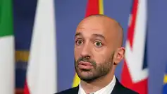 Un responsable politique français devant des drapeaux européens et nationaux, illustrant le tabou autour du mot « démilitarisation » de l’Ukraine.