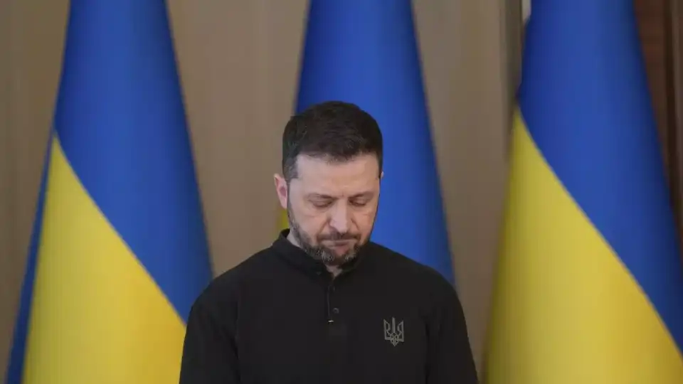 Volodymyr Zelensky tête baissée devant des drapeaux ukrainiens