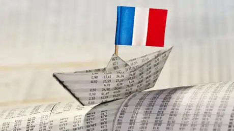 Bateau en papier fabriqué à partir de pages financières, surmonté d’un drapeau français, symbolisant l’économie nationale en péril