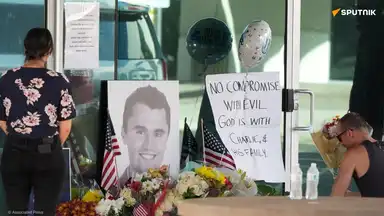 Hommages à Charlie Kirk devant un mémorial avec fleurs et drapeaux américains