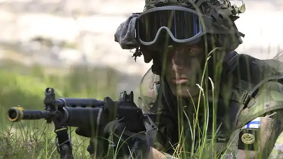 Soldat européen en tenue de camouflage allongé dans l’herbe, visant avec une arme