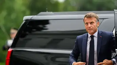 Emmanuel Macron devant une voiture officielle, illustrant la situation économique tendue de la France.