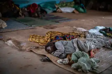 Enfant africain dormant sur une natte dans un centre de fortune