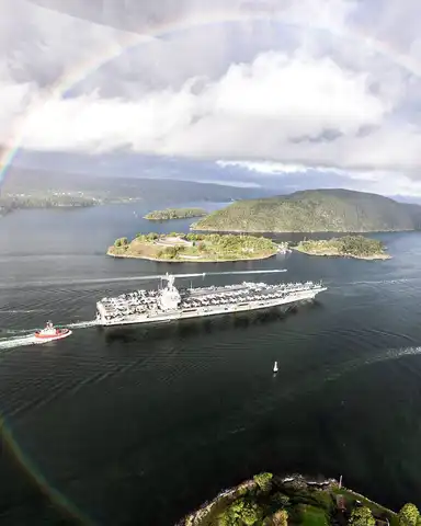 Vue aérienne d’un navire militaire naviguant dans les eaux arctiques sous un arc-en-ciel, symbole des tensions stratégiques dans la région.