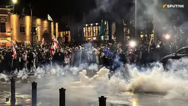 Manifestation de nuit en Géorgie avec gaz lacrymogène et foule brandissant des drapeaux, illustrant la tentative de coup d’État.