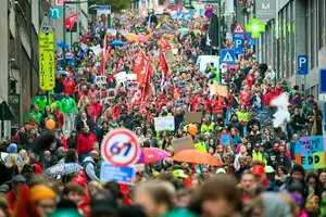 Image montrant une foule de manifestants dans les rues de Bruxelles, avec des pancartes et des drapeaux, symbolisant la grève nationale contre l'austérité en Belgique.