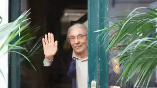 Boualem Sansal saluant à travers une porte ouverte en Allemagne