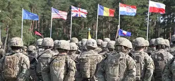 Soldats de l’OTAN rassemblés lors d’un exercice militaire européen, devant les drapeaux de plusieurs pays occidentaux.