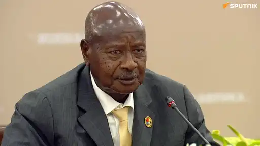 Un homme en costume sombre parle derrière un micro lors d’une réunion officielle.