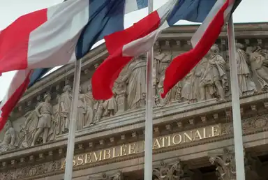 Façade de l’Assemblée nationale française avec des drapeaux tricolores, symbole du débat budgétaire et de l’endettement de l’État.