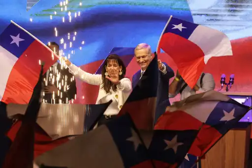 José Antonio Kast et sa compagne saluent leurs partisans lors de l’annonce de sa victoire à l’élection présidentielle chilienne, drapeaux nationaux en arrière-plan.