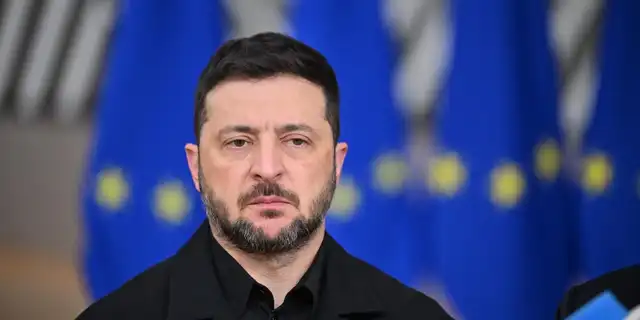 Portrait de Volodymyr Zelensky devant des drapeaux de l’Union européenne, expression sérieuse.