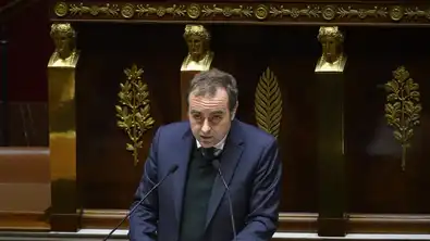 Homme en costume noir parlant devant un micro, illustrant la discussion sur le budget 2026.