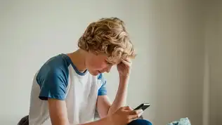 Adolescent assis regardant son smartphone, expression de stress liée aux réseaux sociaux