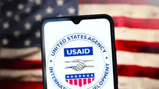 Logo de l'agence USAID sur un smartphone, avec un drapeau américain en arrière-plan.