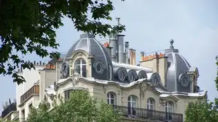 Façade d'un immeuble haussmannien à Paris avec toitures en dôme sous un ciel clair.