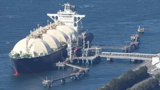 navire méthanier ancré près d'une installation portuaire, chargé de conteneurs cylindriques.