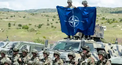 Soldats en uniforme de camouflage sur des blindés déployant le drapeau bleu de l'OTAN.