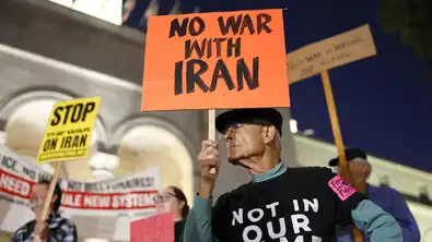 Manifestant âgé tenant une pancarte orange "NO WAR WITH IRAN" lors d'un rassemblement nocturne.