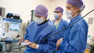 Trois soignants en tenue stérile bleue manipulant du matériel médical dans un bloc opératoire.