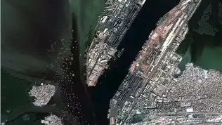 Vue satellite haute résolution de navires de fret traversant un détroit maritime étroit.