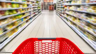 Vue subjective d'un chariot de courses rouge vide dans l'allée floue d'un supermarché.