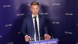 Péter Magyar s'exprimant derrière un pupitre devant un mur aux logos TISZA.