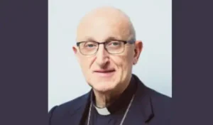 Portrait de Monseigneur Dominique Rey en habit ecclésiastique sur fond gris clair.