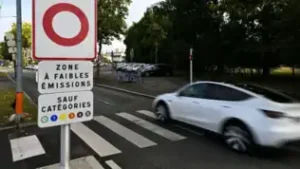 Panneau signalant une Zone à Faibles Émissions à l'entrée d'une rue avec une voiture blanche.