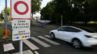 Panneau signalant une Zone à Faibles Émissions à l'entrée d'une rue avec une voiture blanche.
