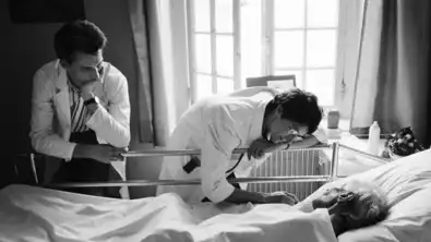 Photo noir et blanc de deux médecins au chevet d'un patient âgé dans un lit d'hôpital.