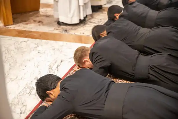 Plusieurs hommes en habit ecclésiastique noir prosternés face contre terre lors d'un rite.