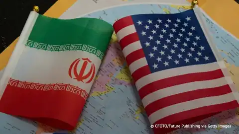 Drapeaux de l'Iran et des États-Unis posés côte à côte sur une carte du monde en arrière-plan.