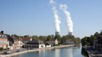 Deux grandes tours de refroidissement nucléaire émettant de la vapeur blanche derrière un canal.