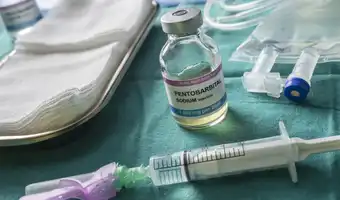 Vue rapprochée d'un vial de Pentobarbital Sodium et d'un used syringe sur un champ opératoire.