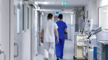 Deux soignants de dos marchant dans le couloir blanc et stérile d'un centre hospitalier moderne.