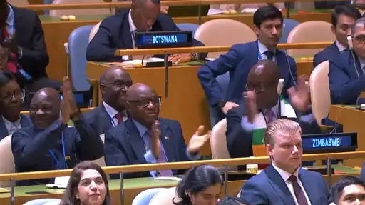Officiels applaudissant à l’ONU derrière un panonceau au nom du Zimbabwe en assemblée