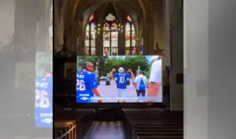 Écran géant retransmettant un reportage sportif au milieu de la nef de l'église de Ligny-en-Barrois.