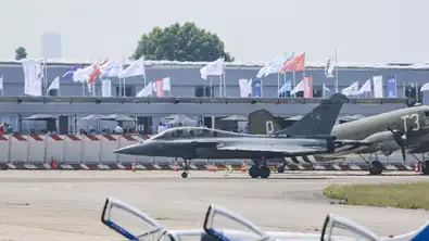 Chasseur Rafale français au sol lors d'un salon aéronautique devant des pavillons et des drapeaux.