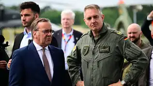 Plan moyen du chef de la Luftwaffe en combinaison de vol kaki aux côtés de responsables politiques en costume.