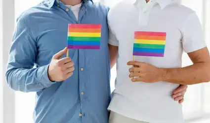 Plan moyen de deux hommes en chemise et polo tenant de petits drapeaux arc-en-ciel devant leur torse.