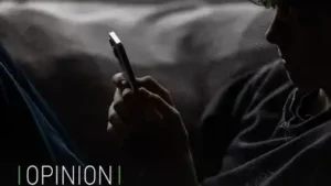 Un adolescent de profil dans la pénombre, captivé et éclairé par l'écran de son smartphone.