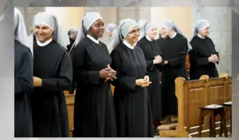 Groupe de religieuses en habit noir et voile gris souriant à l'intérieur d'une église catholique.
