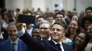 Emmanuel Macron souriant prenant un selfie au smartphone au milieu d'une foule lors d'un rassemblement.