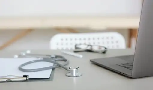 Un stéthoscope posé sur un bureau médical à côté d'un dossier patient et d'un ordinateur portable.