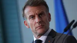 Emmanuel Macron à la tribune d'un sommet de l'OTAN sur fond de drapeaux de l'Alliance atlantique.